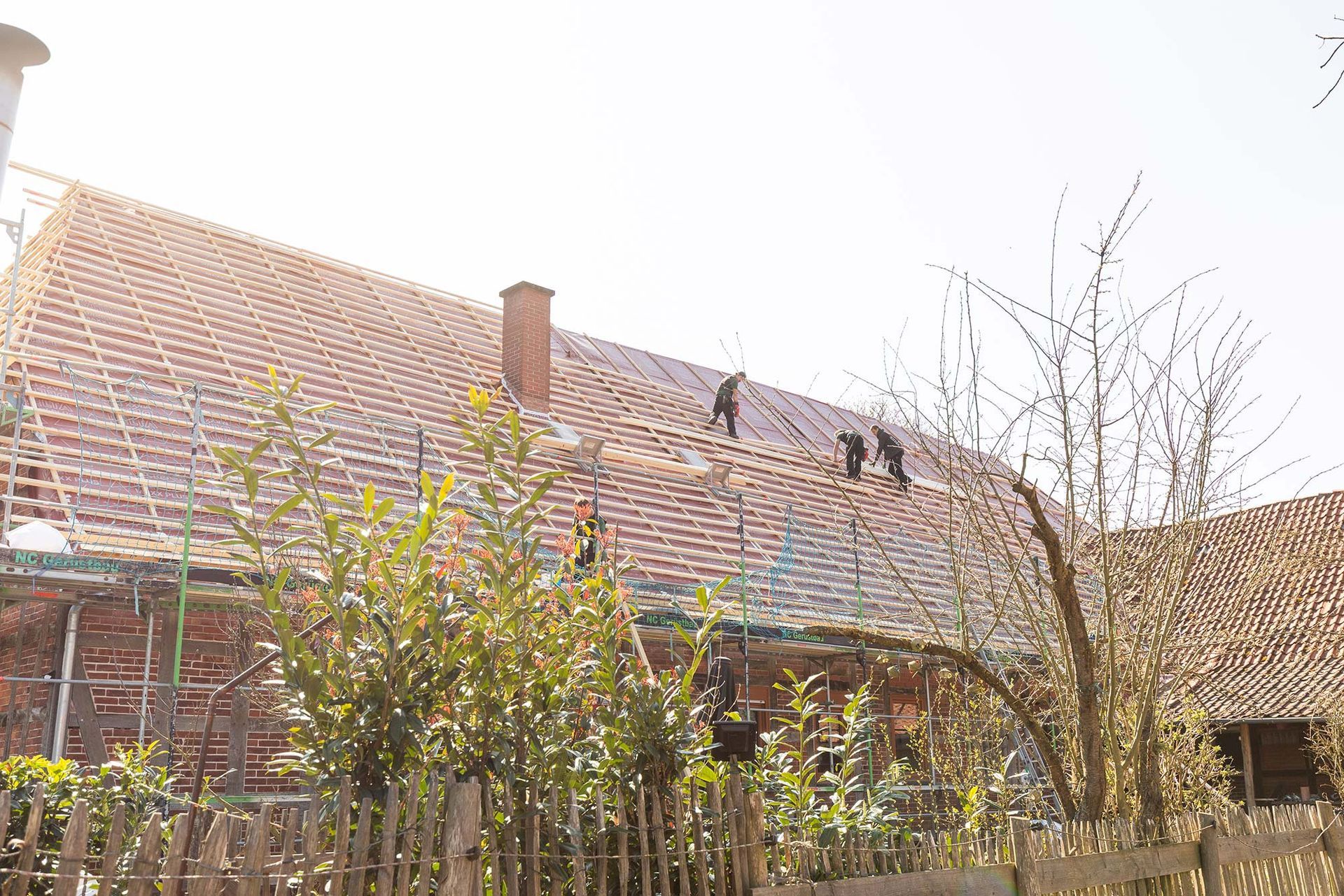 Ein Backsteinhaus mit einem im Bau befindlichen Dach und einem Holzzaun davor.