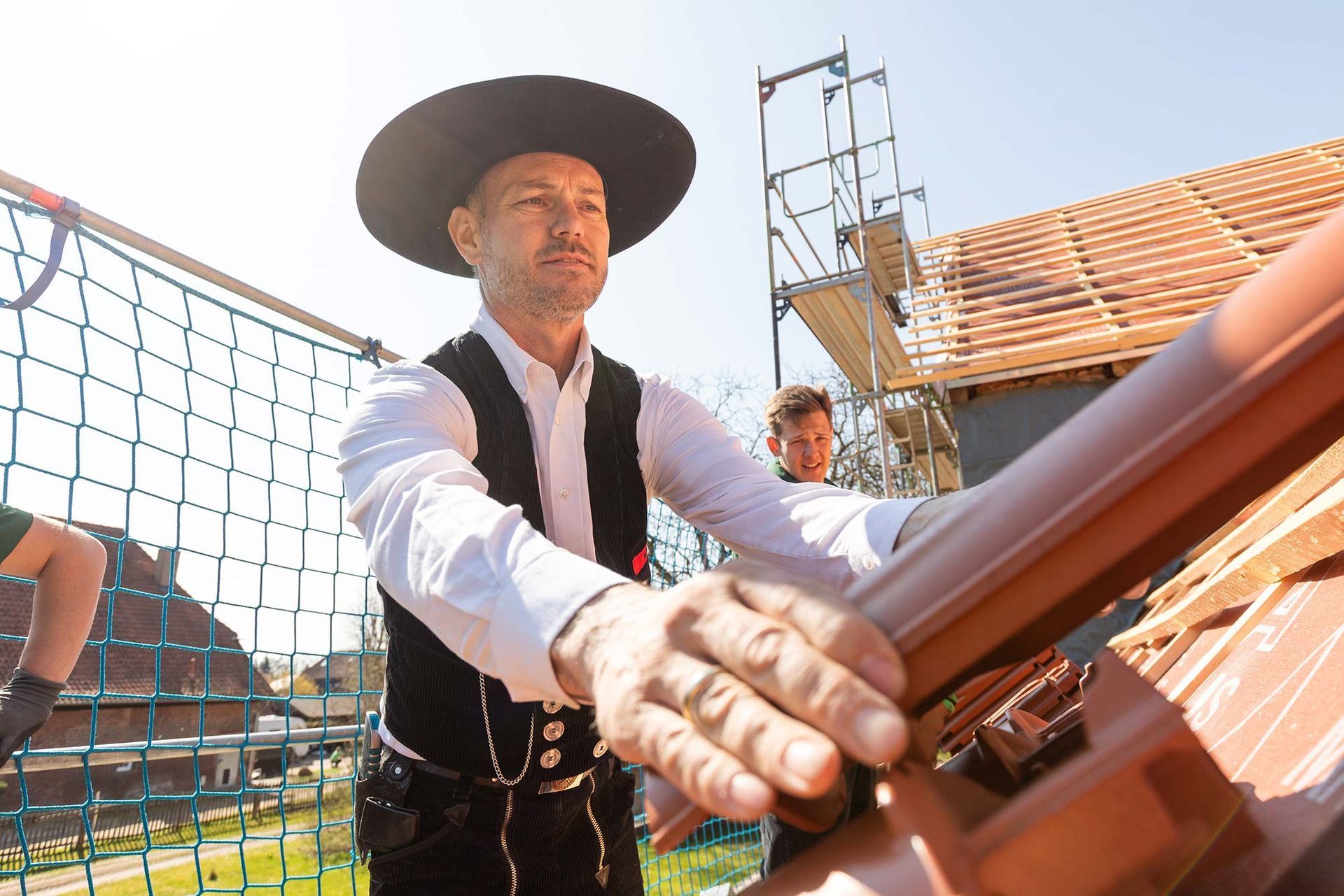 Ein Mann mit Hut arbeitet auf einem Dach.