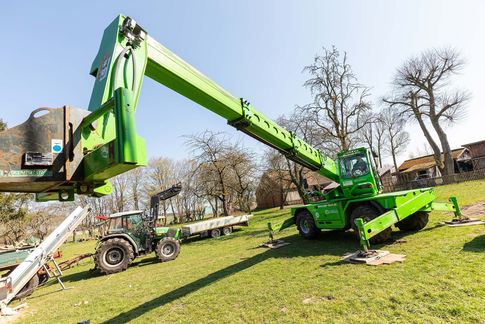 Auf einer Wiese steht ein grüner Kran auf einem Traktor.