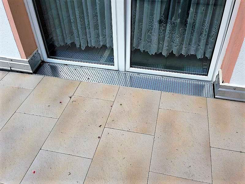 Auf einem gefliesten Boden neben einem Fenster befindet sich eine Glasschiebetür.