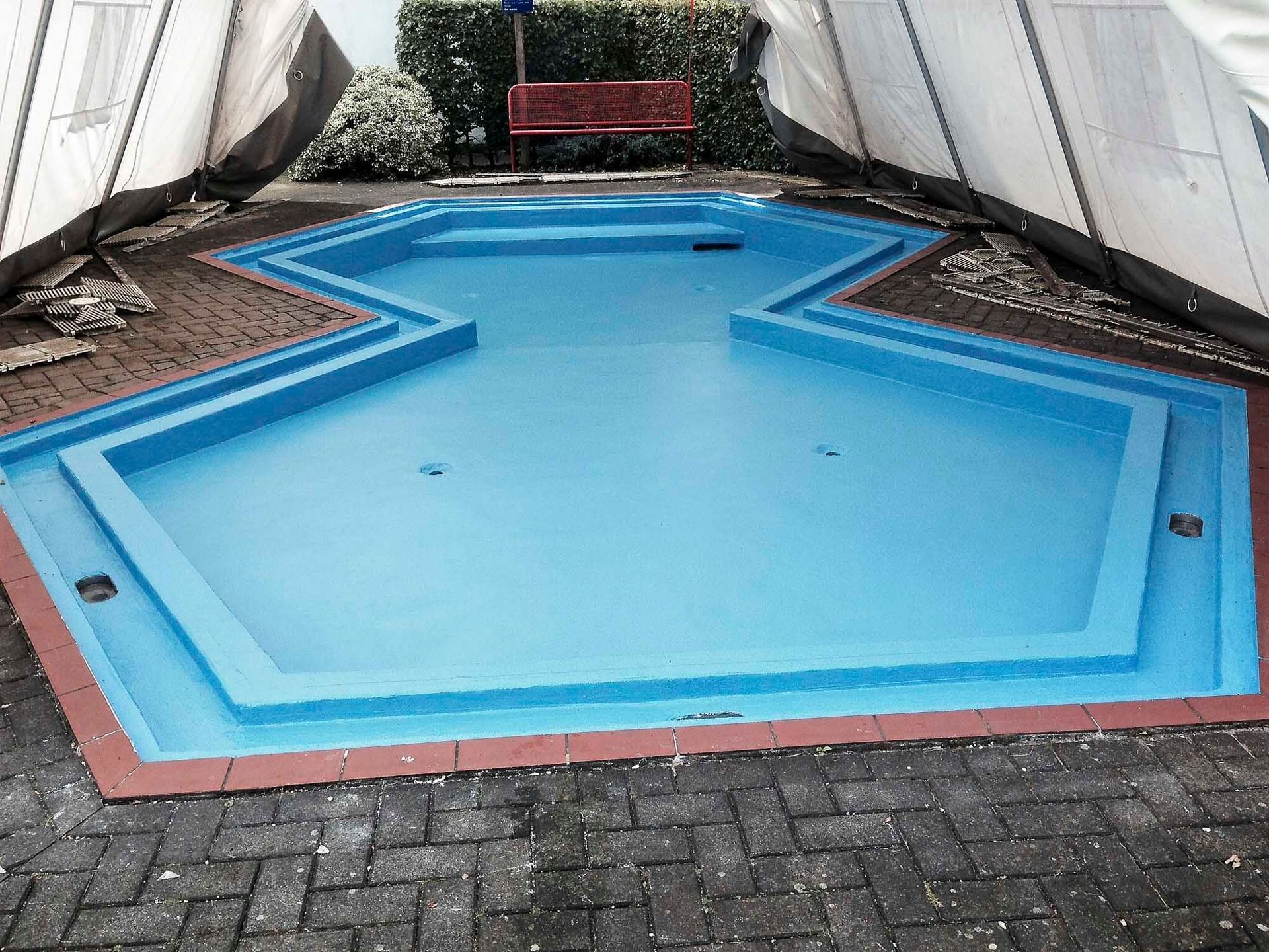 Auf einer gemauerten Terrasse steht ein blauer Pool mit rotem Rand.