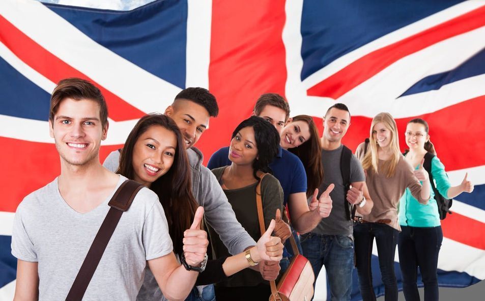 Personas sonrientes de pie juntas frente a una gran bandera británica, levantando el pulgar.