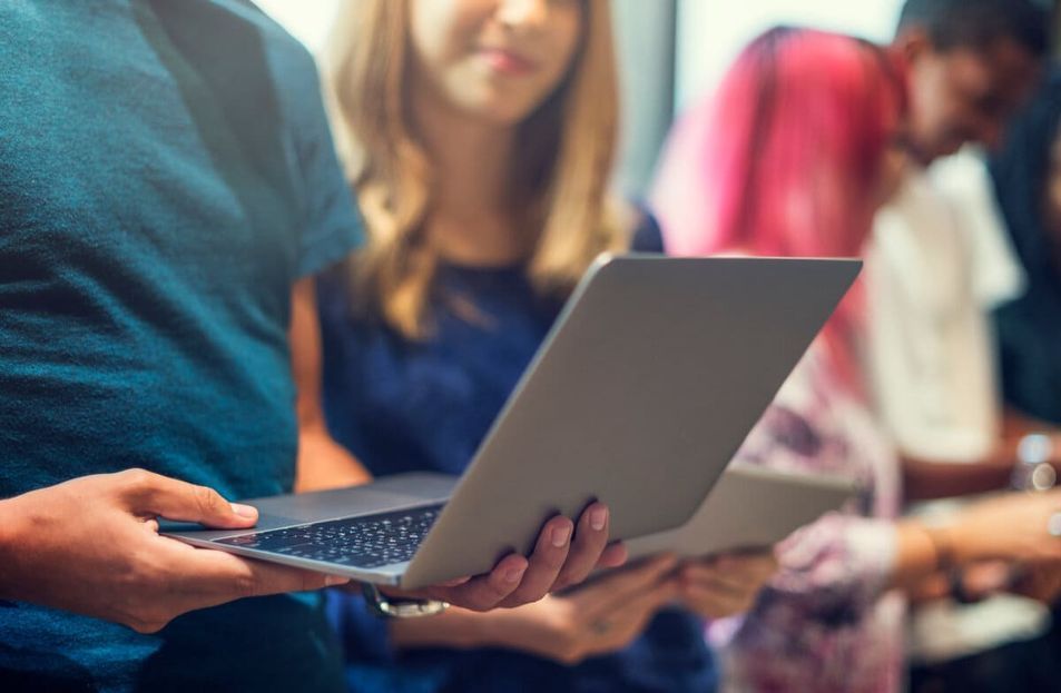 Personas de pie juntas, sosteniendo computadoras portátiles en un entorno interior concurrido.