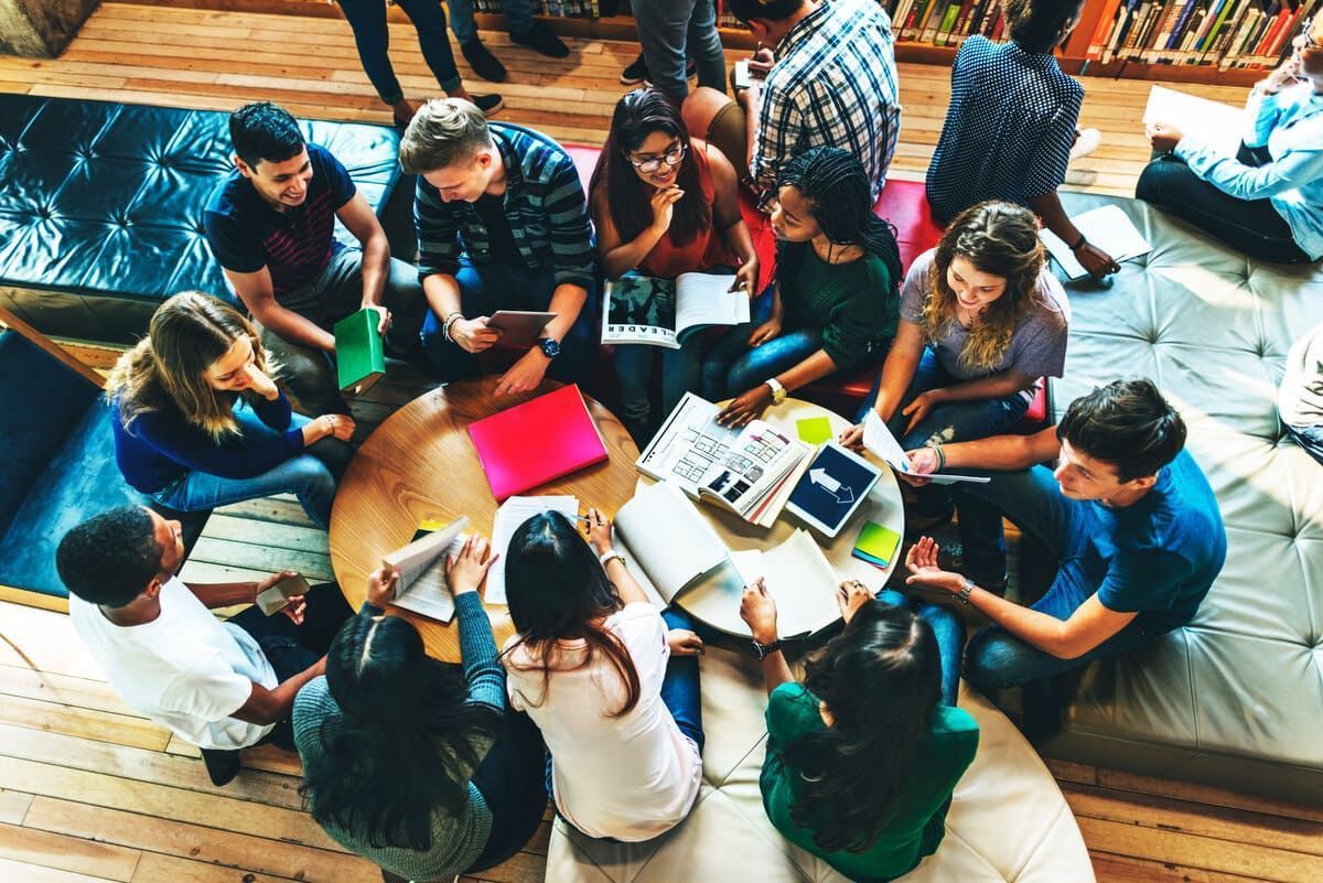 Un grupo de personas sentadas en círculo en el suelo, colaborando con ordenadores portátiles y libretas en un espacio de trabajo informal.