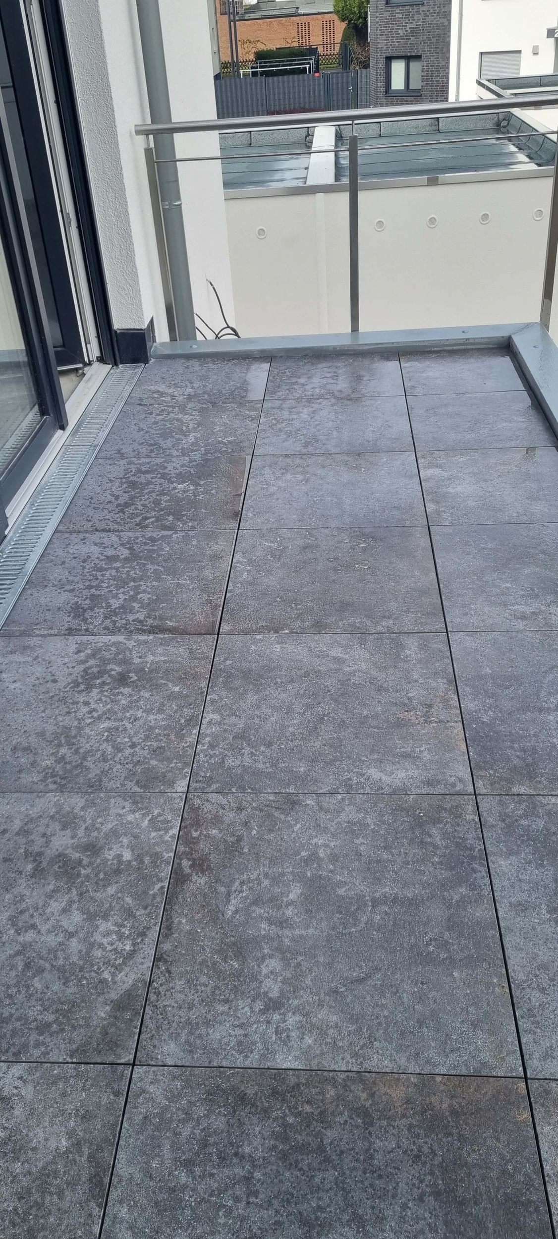 Ein Balkon mit grauem Fliesenboden und einem Geländer aus Edelstahl.