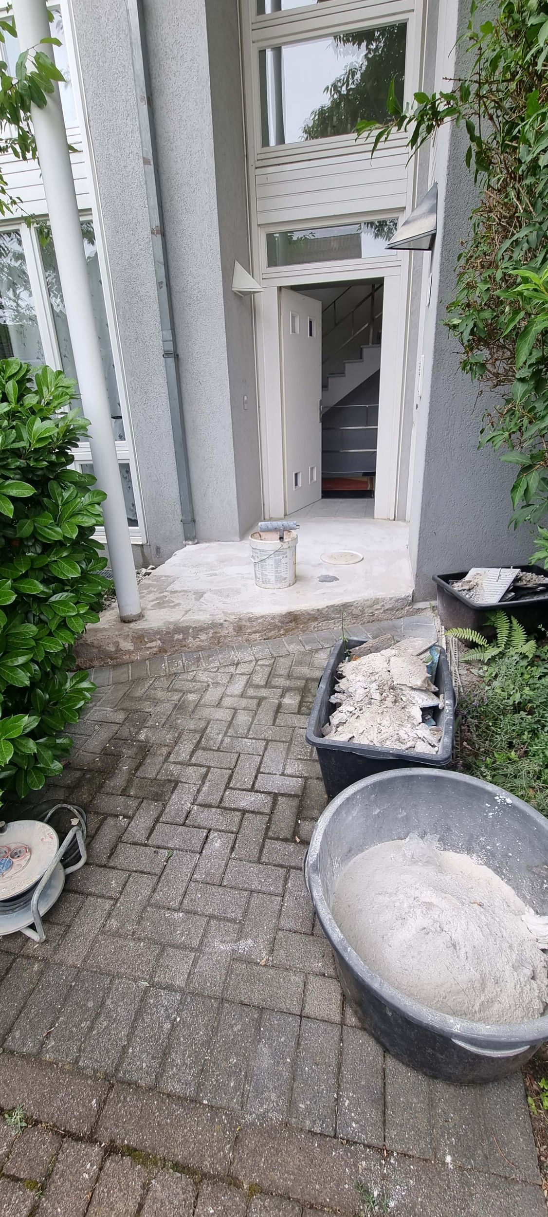 Ein gemauerter Gehweg mit Eimern voller Sand und Zement vor einem Gebäude.