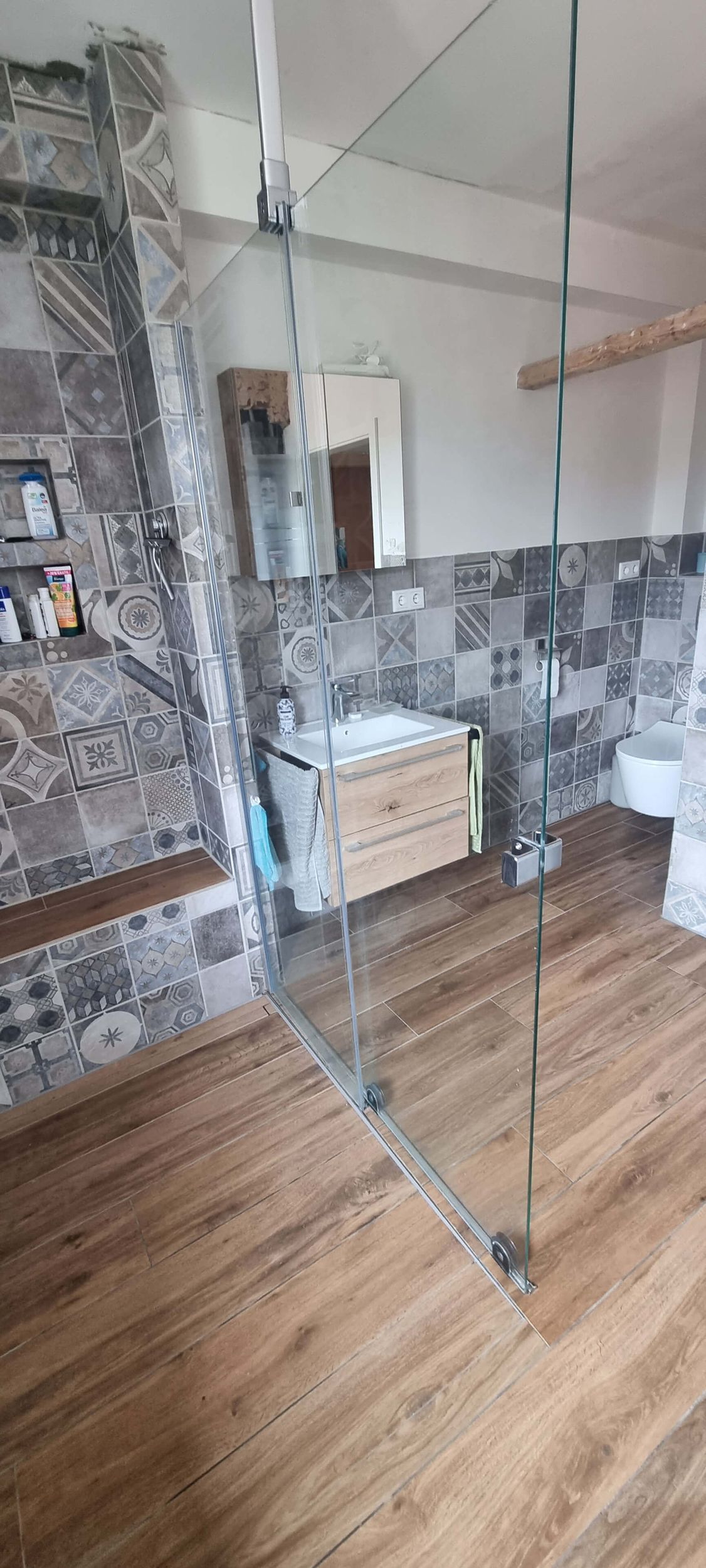 Ein Badezimmer mit ebenerdiger Dusche, Waschbecken, Toilette und Spiegel.