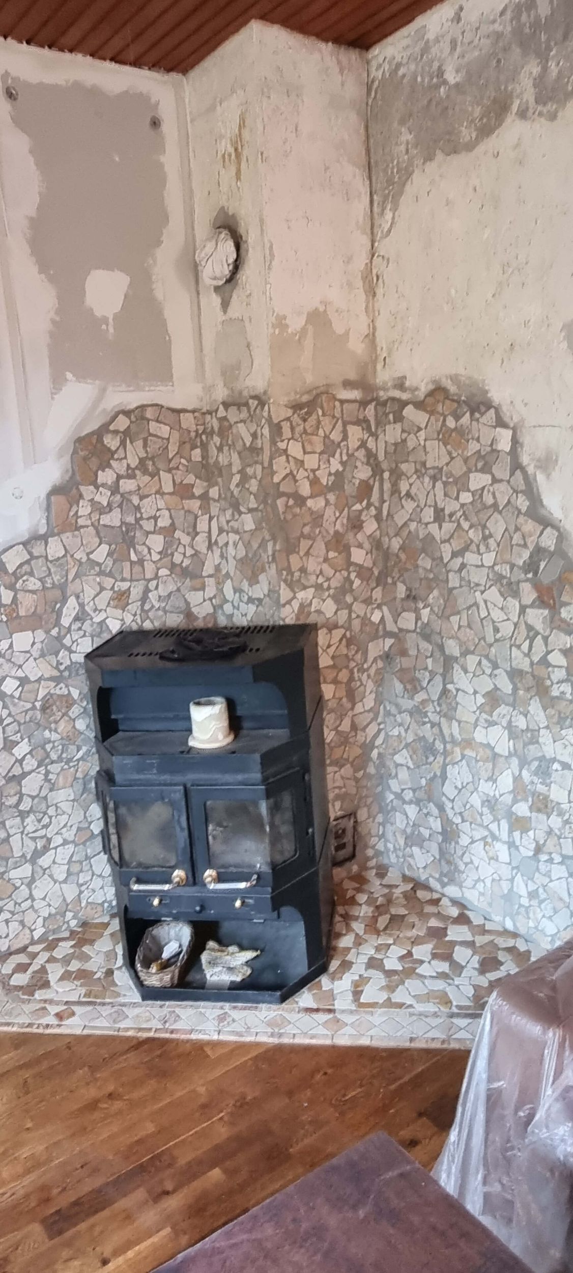 In der Ecke eines Wohnzimmers steht neben einer Steinmauer ein Holzofen.