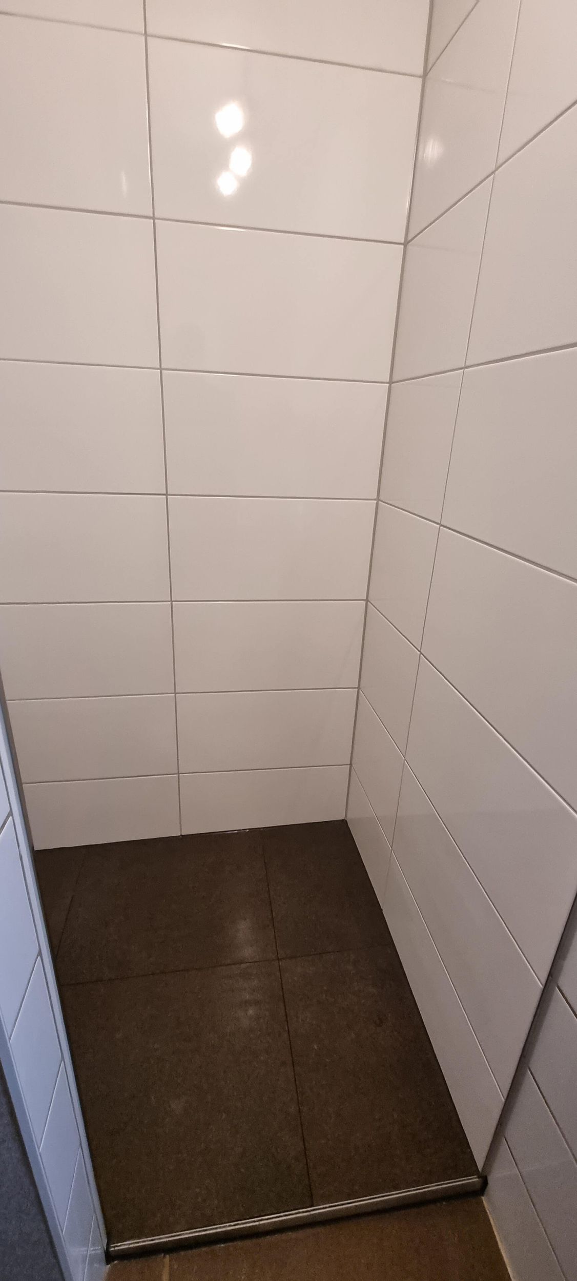 Ein Badezimmer mit weißen Fliesen und braunem Boden.