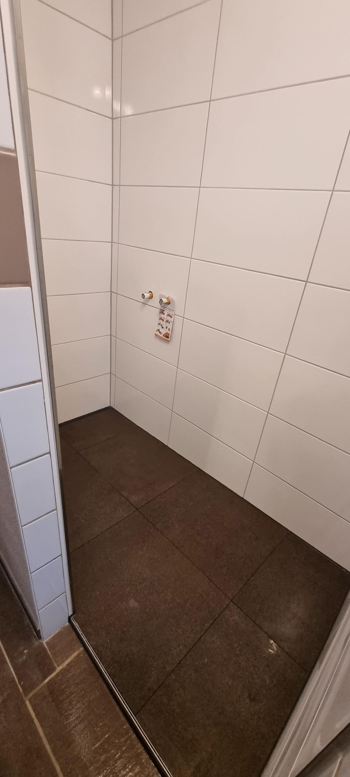 Ein Badezimmer mit weißen Fliesen und braunem Boden.