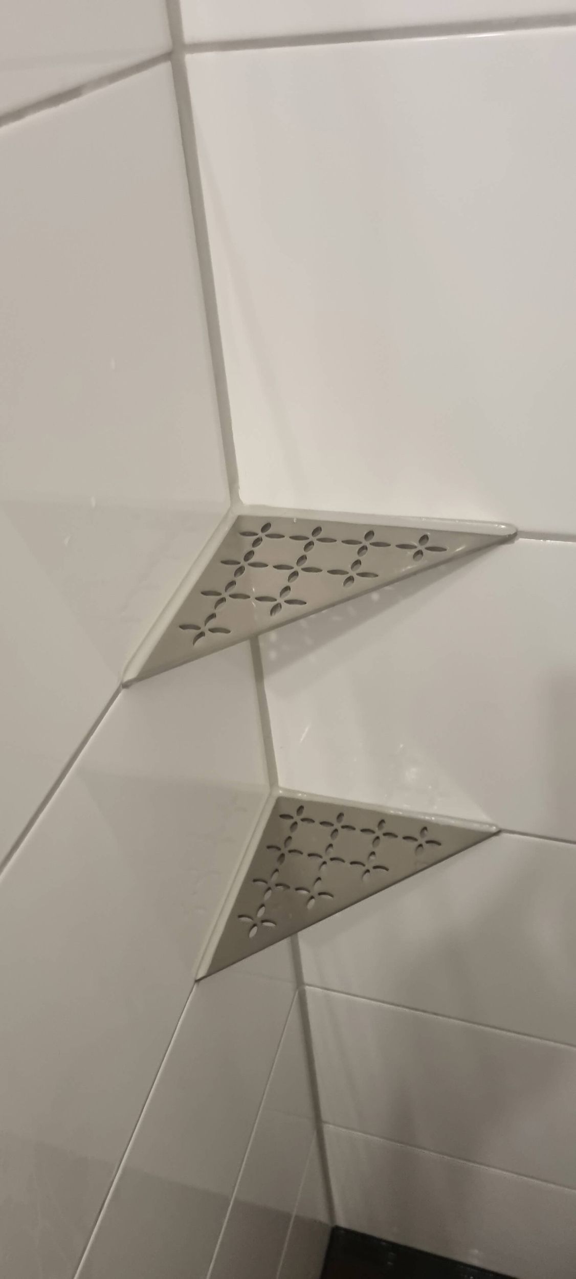 Ein Badezimmer mit weißen Fliesen und einem Eckregal.