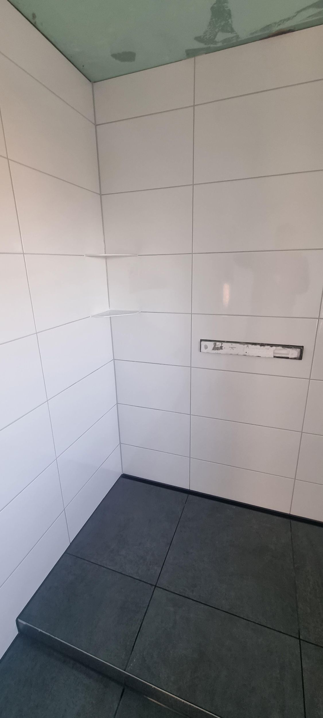 Ein Badezimmer mit weißen Fliesen und schwarzem Boden.