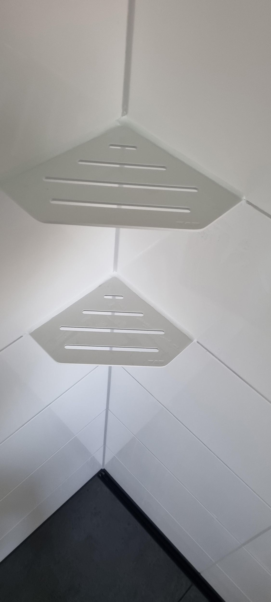 In einem Badezimmer hängen zwei weiße Eckregale von der Decke.