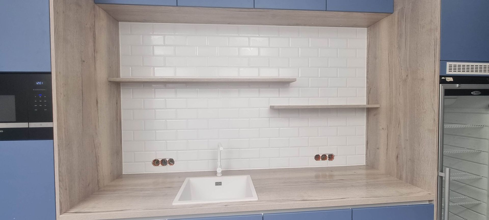 Eine Küche mit blauen Schränken, einer Spüle, einer Mikrowelle und Regalen.