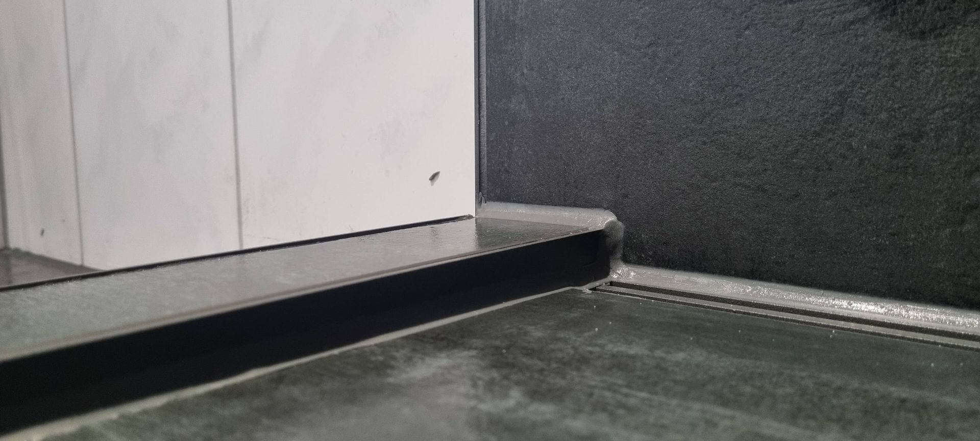 Eine Raumecke mit einer schwarzen Wand und einem Betonboden.