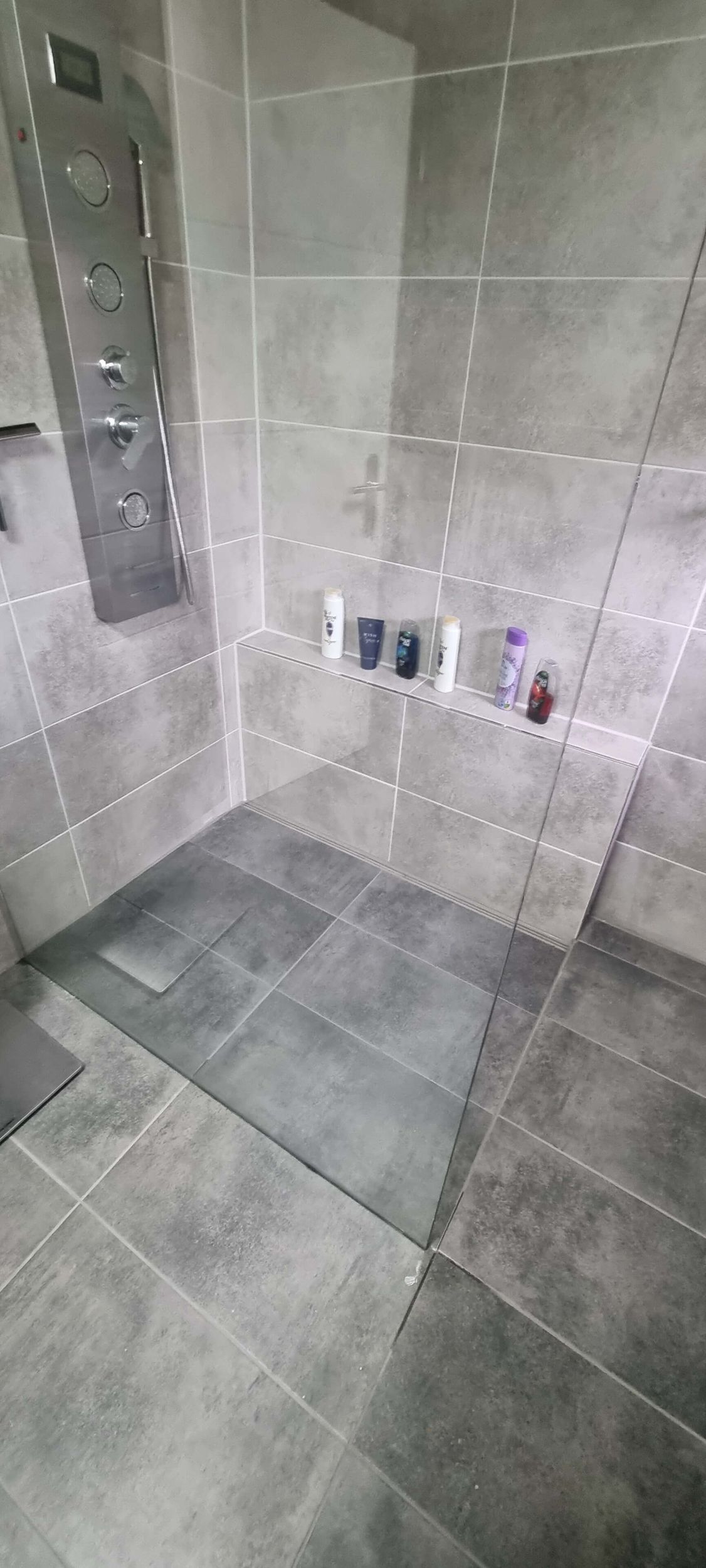 Ein Badezimmer mit grauen Fliesen und einer ebenerdigen Dusche.