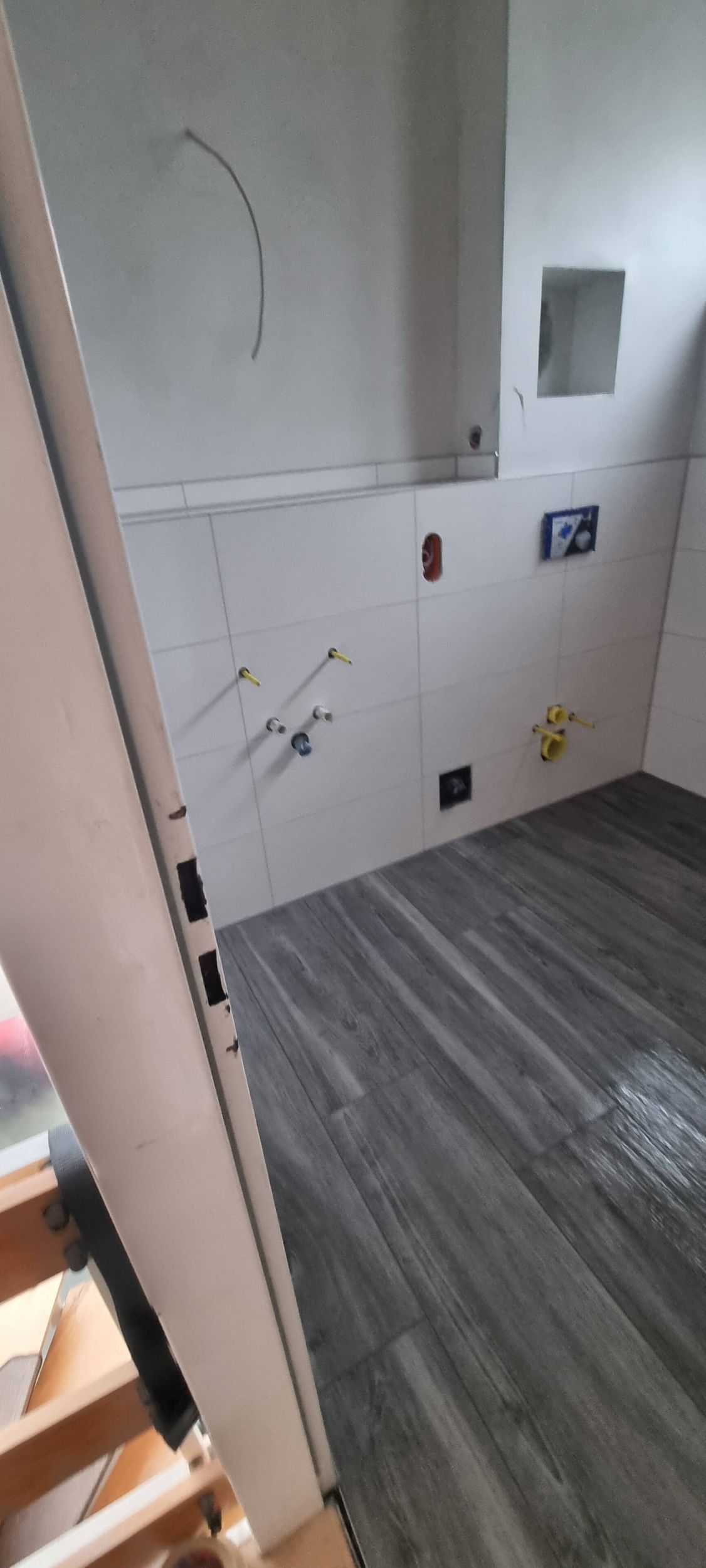 Ein im Bau befindliches Badezimmer mit Holzboden und weißen Fliesen.