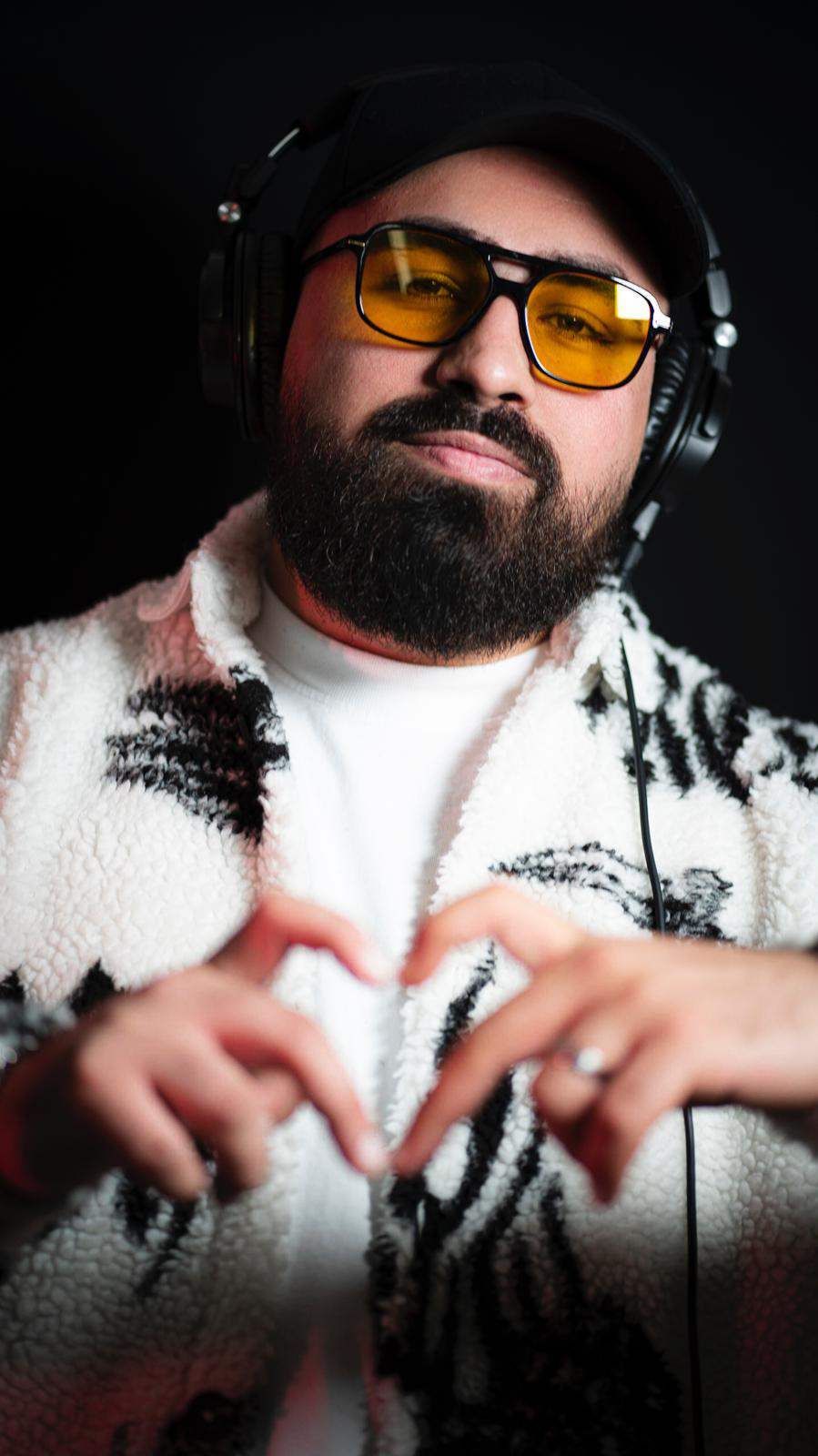 Ein Mann mit Bart, Kopfhörern und Sonnenbrille formt mit seinen Händen ein Herz.