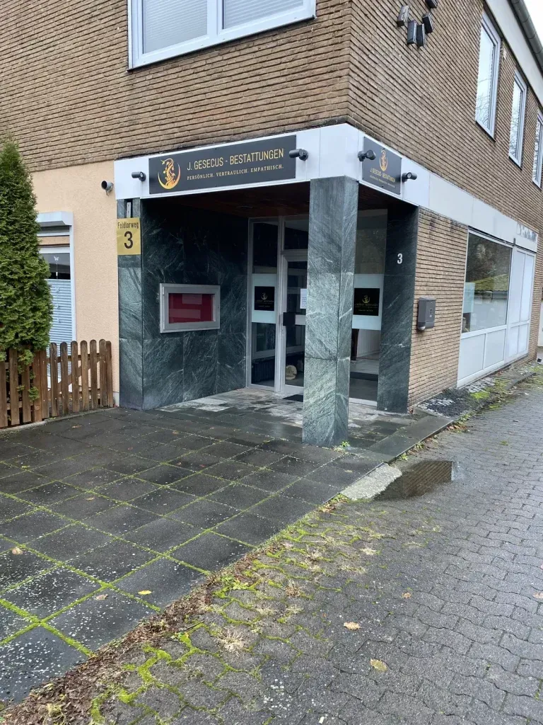 Eingang zu einem Gebäude mit grüner Fassade und einem Schild über der Tür; einem Bürgersteig und einem kleinen Zaun.