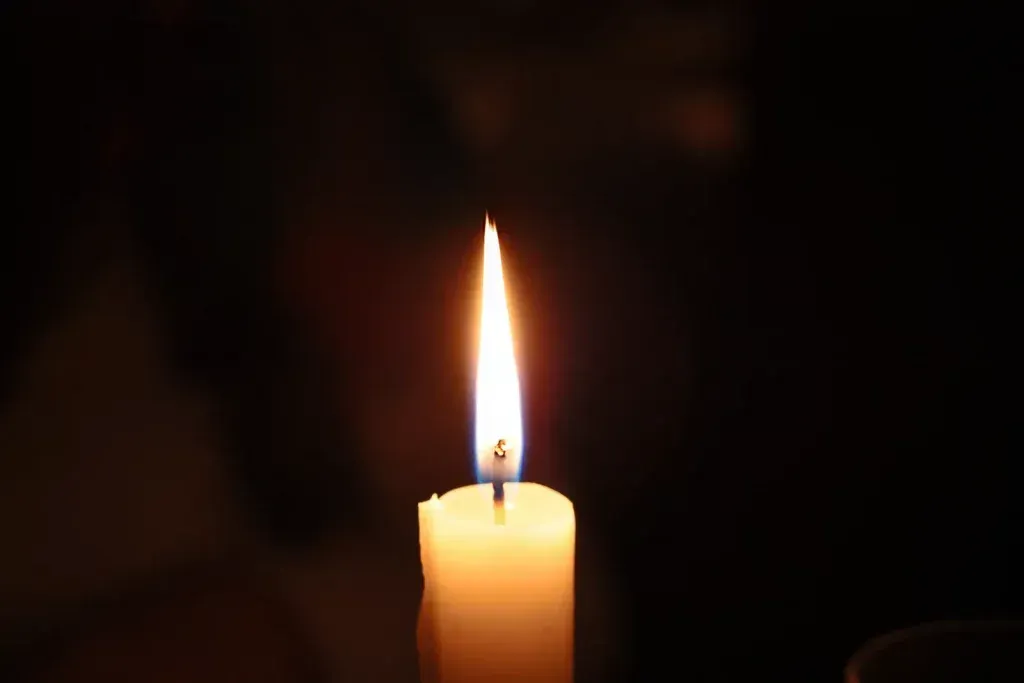 Brennende Kerze mit leuchtend orangefarbener Flamme vor dunklem Hintergrund.