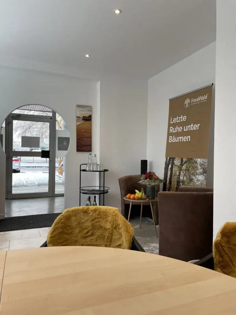 Innenansicht: Ein moderner, heller Raum mit Sitzgelegenheiten, einem Tisch und einem nach draußen führenden Rundbogen.