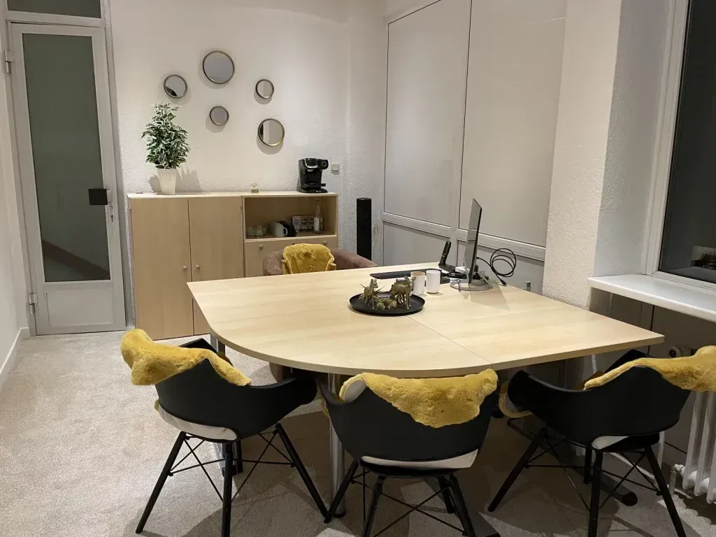 Esszimmer mit einem Holztisch, schwarzen Stühlen mit gelben Schaffellen und einem Schrank mit Spiegeln.