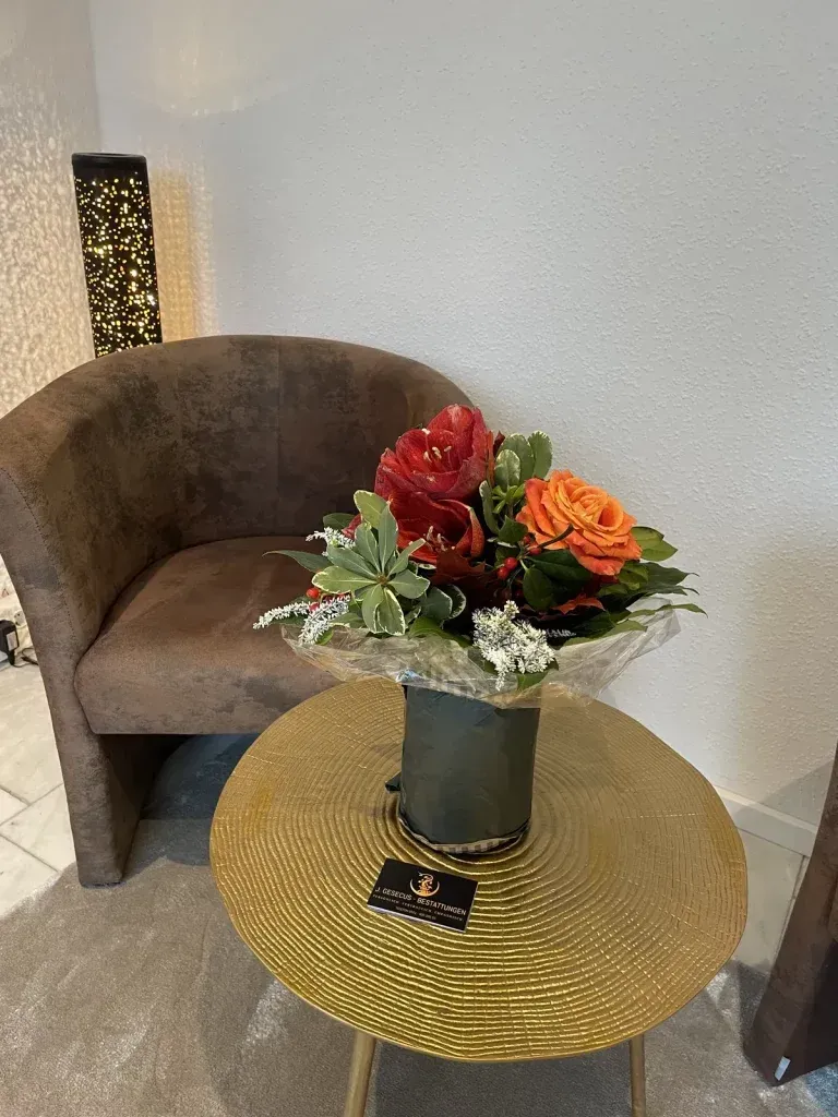 Brauner Sessel neben einem kleinen, goldenen Tisch mit Blumenarrangement vor einer weißen Wand.