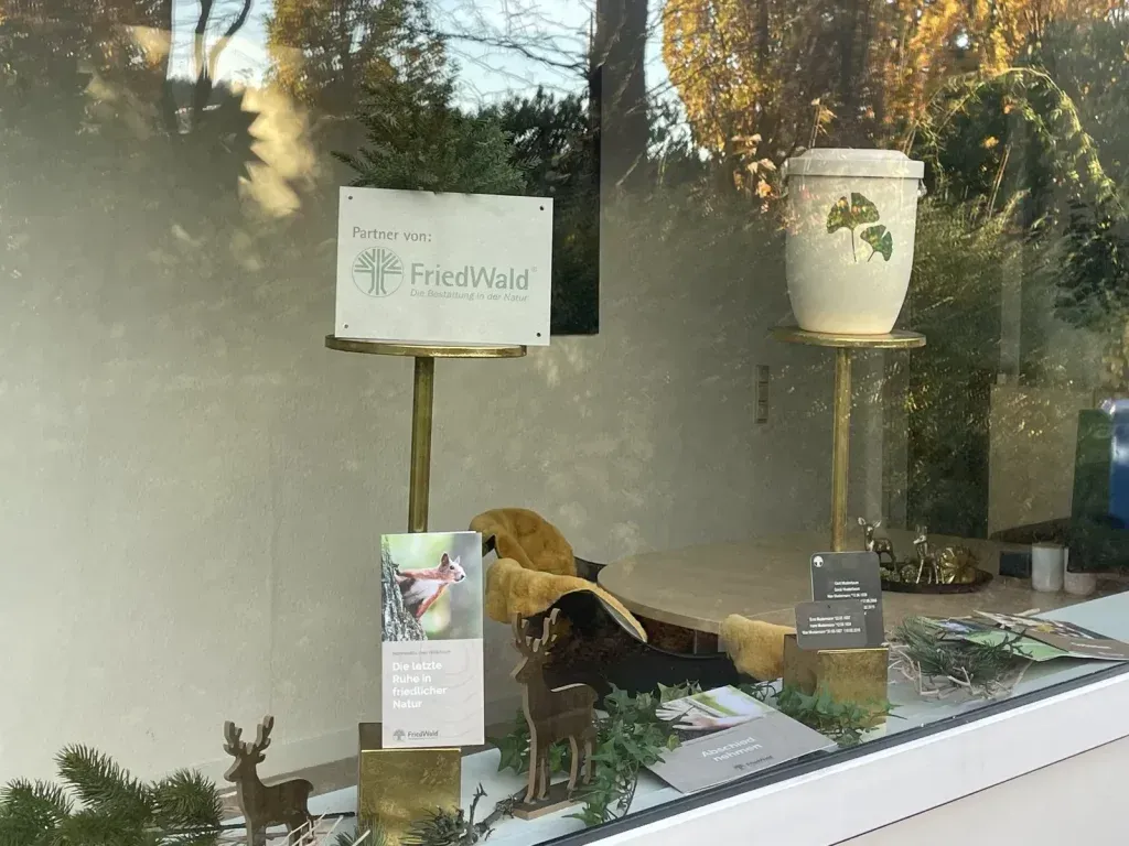 Schaufensterdekoration mit Schild „Feldheim“, Urne, Hirschfiguren und Broschüren.