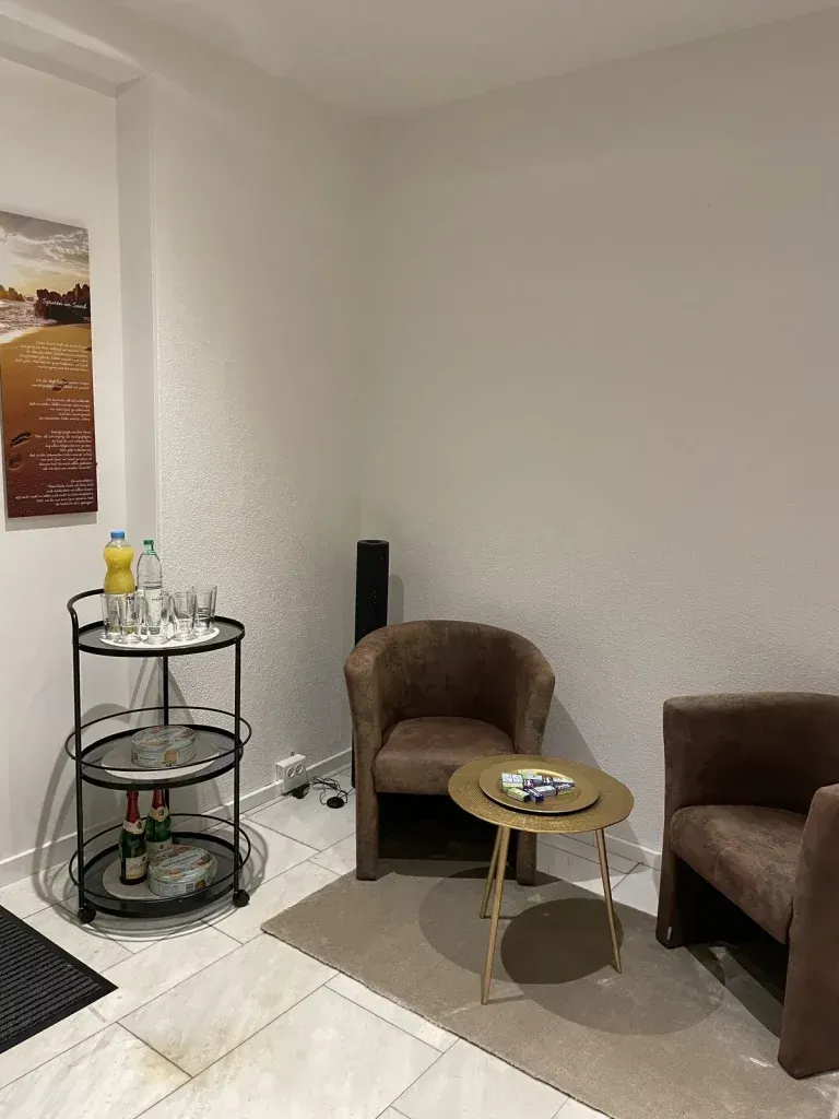 Eine kleine Sitzecke mit zwei braunen Sesseln, einem runden Beistelltisch und einem Barwagen mit Getränken.