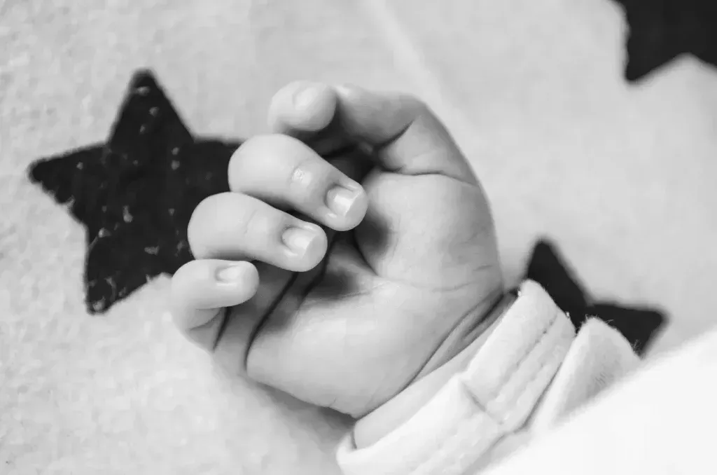 Die Hand des Babys ist zur Faust geballt und ruht auf einer Decke mit Sternenmuster. Schwarz und weiß.