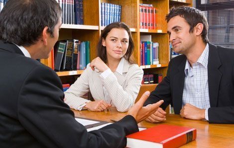 Un hombre y una mujer están sentados en una mesa hablando con un hombre en una biblioteca.