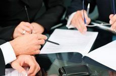 Un grupo de personas está sentada en una mesa firmando un documento.