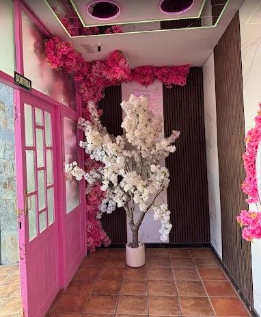 Pasillo rosa con un árbol blanco en flor como elemento central, suelo de baldosas y luces decorativas en el techo.
