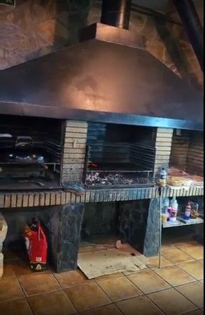 Gran parrilla de ladrillo con campana metálica en una zona de cocina interior alicatada.
