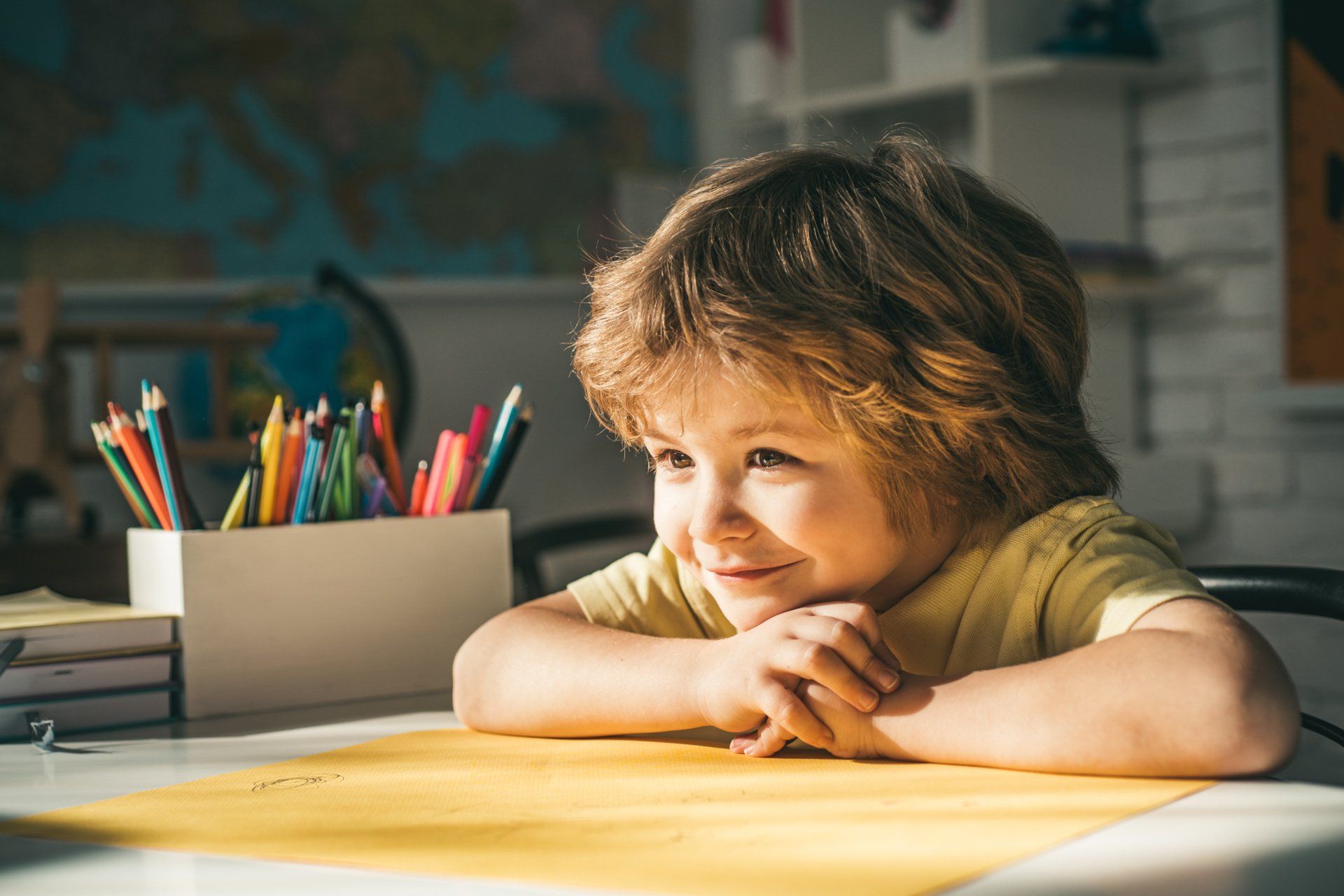 Enfant souriant sur une table avec des crayons à dessin