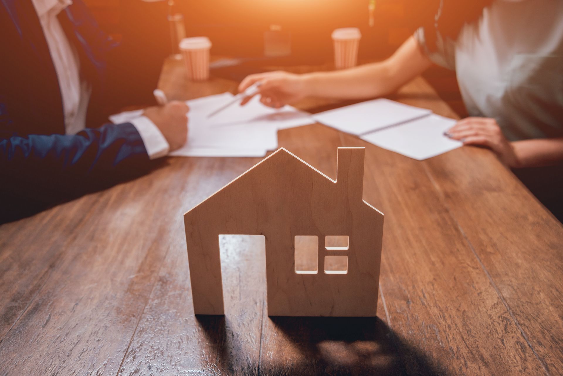 Une maison en bois posée sur le bureau de deux avocats en train de discuter