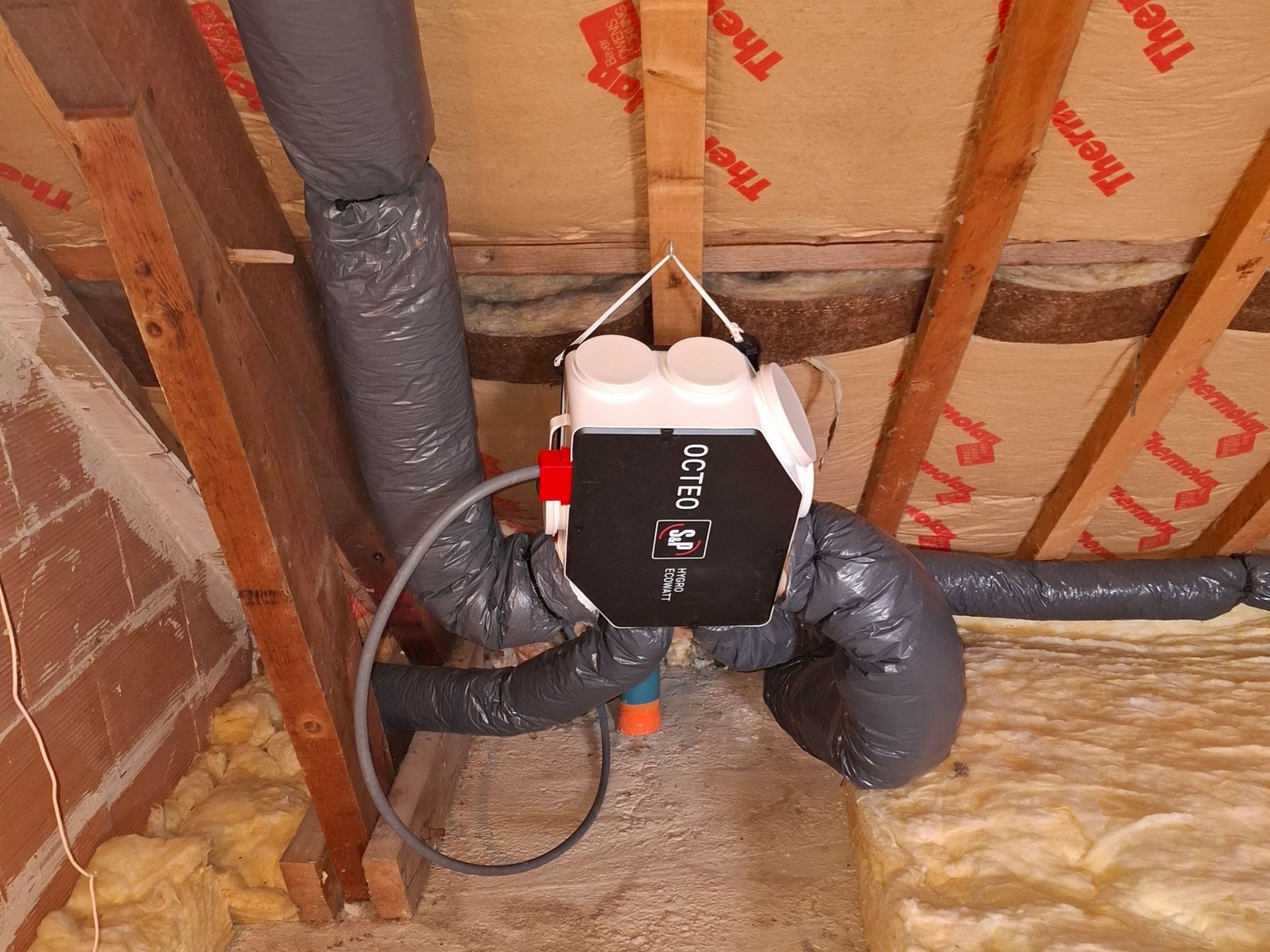 Un grenier isolé, avec des conduits entourant un système de ventilation fixé aux chevrons.
