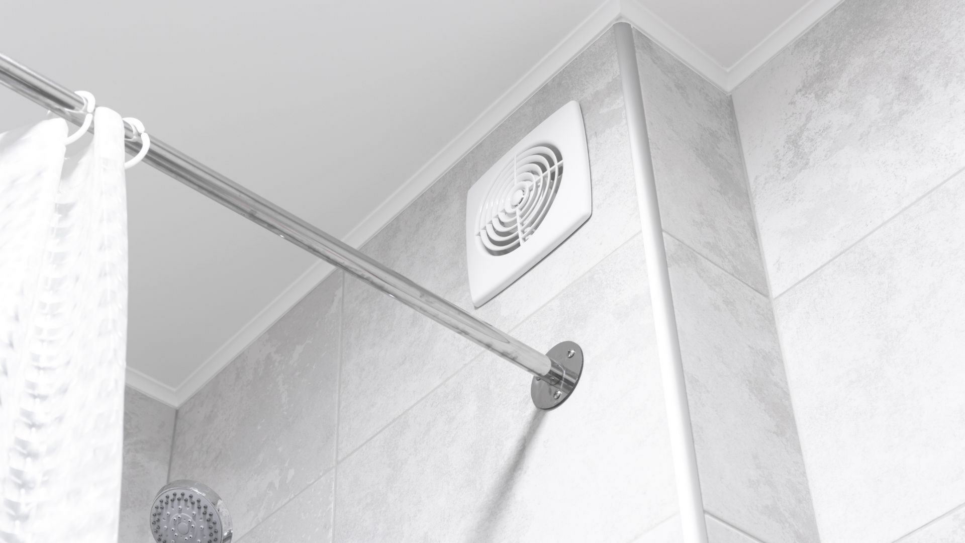 Coin de salle de bain avec barre de douche, ventilateur d'extraction et murs carrelés.