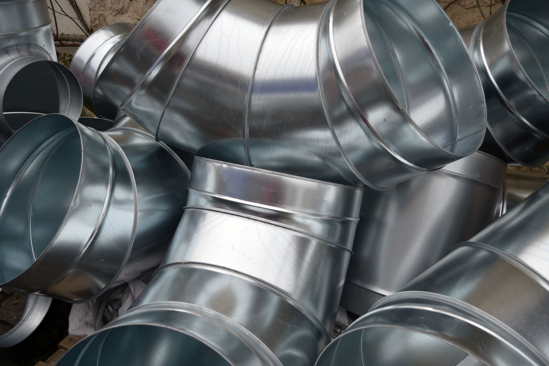 Raccords de conduits en acier galvanisé, de formes diverses, empilés les uns sur les autres.