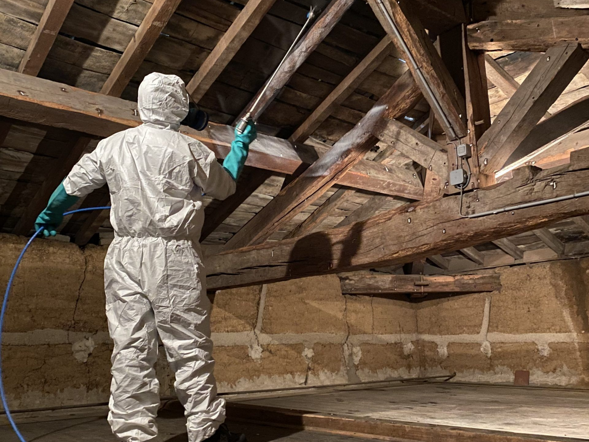 Personne en combinaison de protection pulvérisant un grenier poussiéreux.