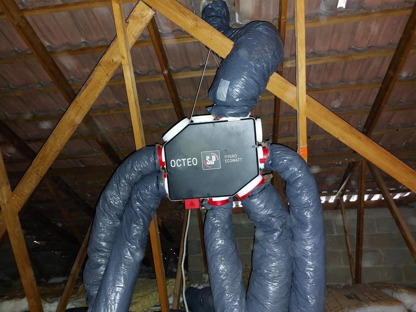 Système de ventilation de combles en noir et blanc suspendu aux chevrons. Des conduits foncés sont reliés à une unité centrale.