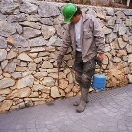 Un hombre que lleva un casco verde está pintando algo sobre una pared de piedra.