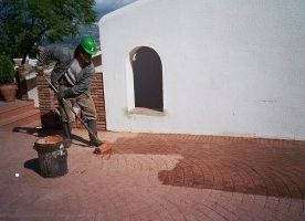 Un hombre está pintando un piso de ladrillo frente a un edificio blanco.