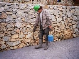 Un hombre que lleva un casco verde está parado frente a un muro de piedra.