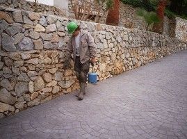 Un hombre que lleva un casco verde camina por una acera junto a un muro de piedra.