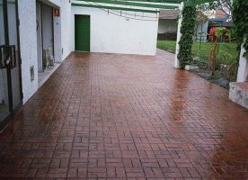 Un camino de entrada de ladrillo con una puerta verde y un edificio blanco al fondo.