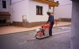 Un hombre está usando una máquina para cortar el asfalto al costado de la carretera.