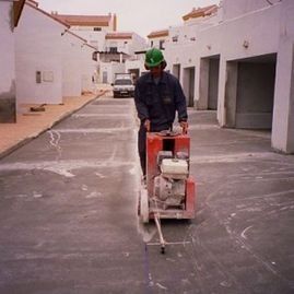 Un hombre que lleva un casco verde está utilizando una máquina para cortar asfalto.