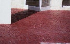 Un suelo de hormigón rojo con una puerta blanca al fondo.