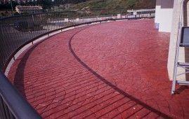 Un balcón con suelo de ladrillo rojo y barandilla negra.